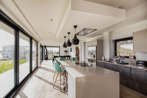 A modern kitchen with white minimalist units and a full length wide French door openinmg onto a patio area