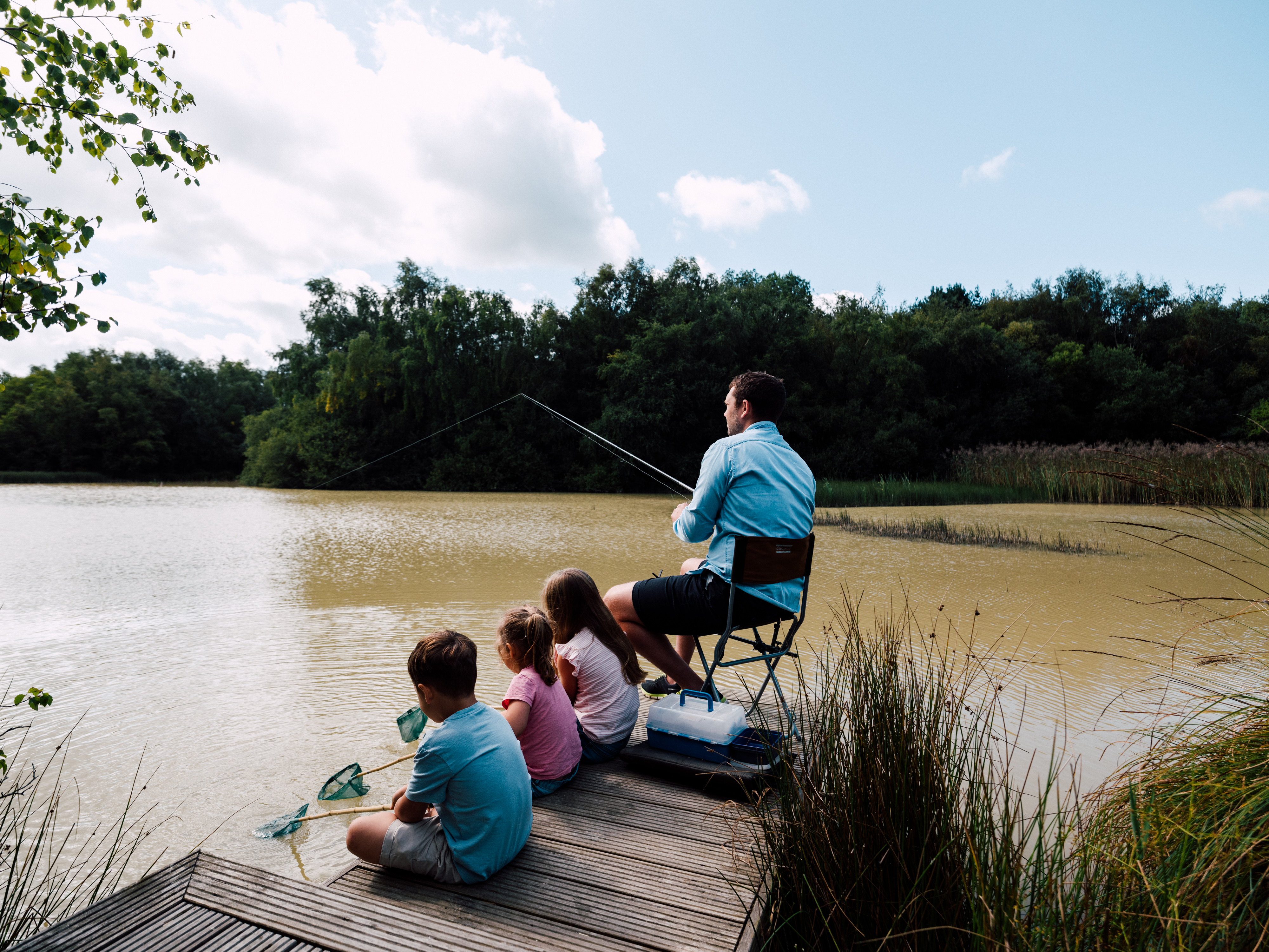 Three children and an adult fishing by a lake