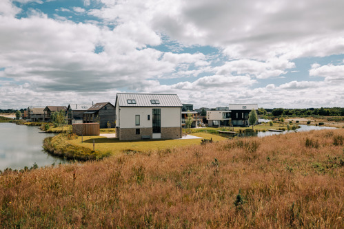 View of a detached house with area of shrubland in the front and a lake to the left