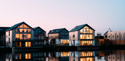 View of four houses on a still lake at dusk with their lights on
