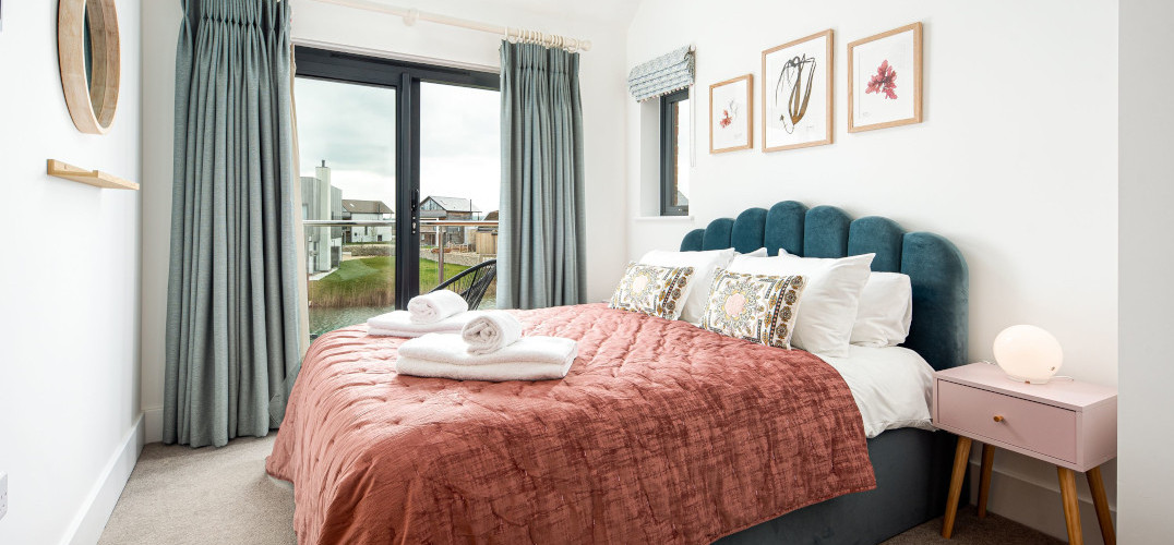 A bedroom containing a bed with a pink bedspread and towels on top
