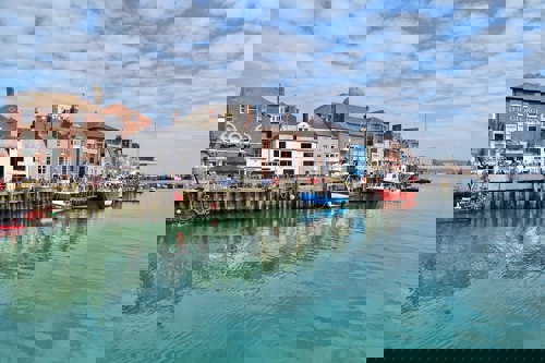 Colourful Weymouth Harbour with little boats on the calm waters and old buildings along the harbour wall