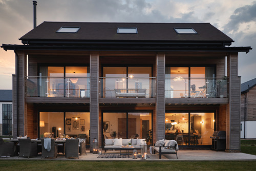 Looking at the front of an inviting holiday home with large windows and al the lights on.